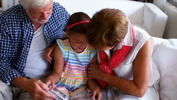 Бабушка с дедушкой и внучка смотрят фотоальбом — стоковое видео