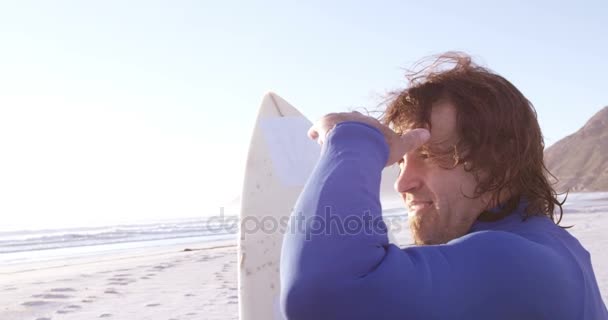 Surfer met surfboard afscherming ogen op strand — Stockvideo