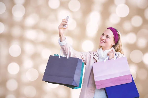 Composite image of smiling woman with shopping bags taking selfies — Stock Photo, Image