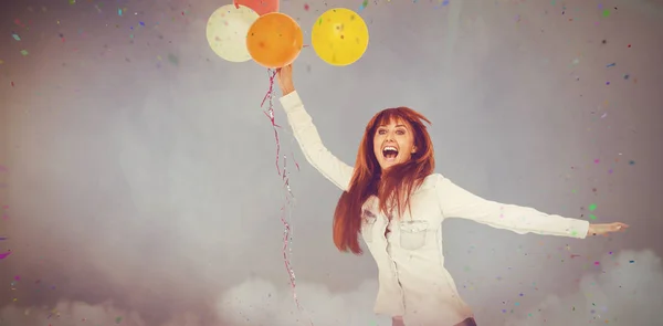 Imagen compuesta de una mujer hipster sonriente sosteniendo globos — Foto de Stock
