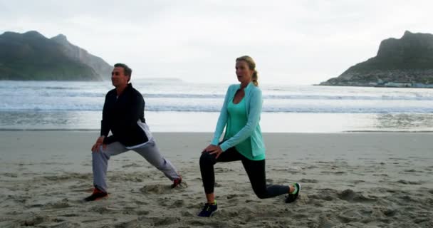 Зрелая пара, выполняющая упражнения на растяжку на пляже — стоковое видео