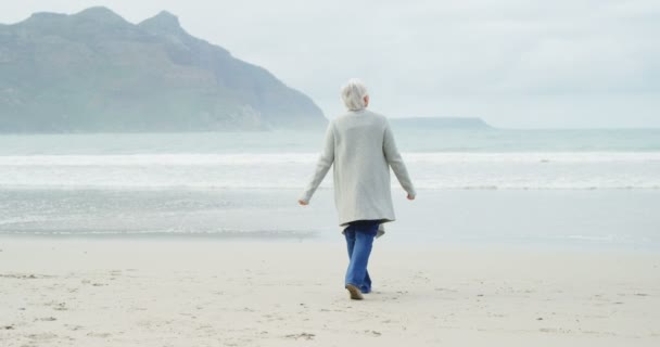 Пожилая женщина, гуляющая по пляжу — стоковое видео