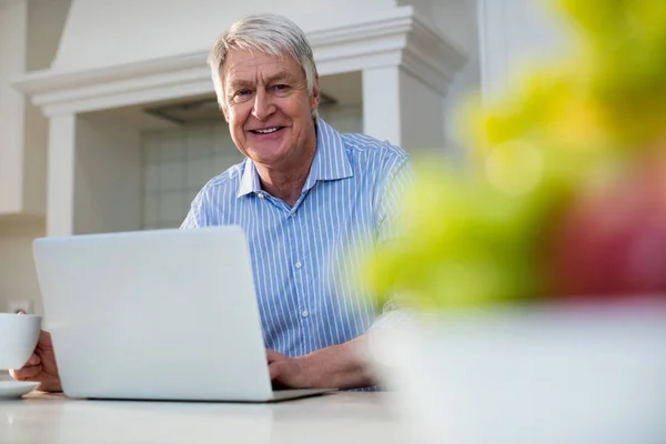 Uomo anziano utilizzando il computer portatile in cucina — Foto Stock