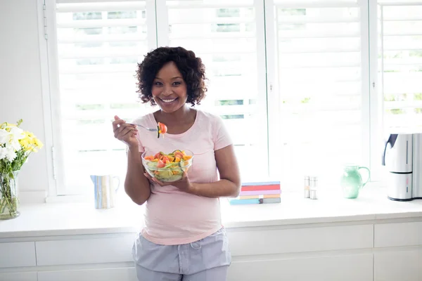 Mujer sonriente comiendo ensalada en la cocina —  Fotos de Stock