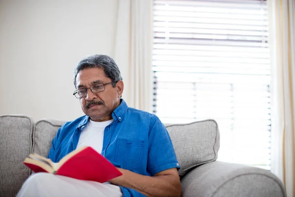 Hombre mayor con gafas leyendo novela — Foto de Stock