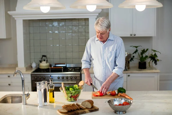 Senior man snijden groenten voor salade — Stockfoto