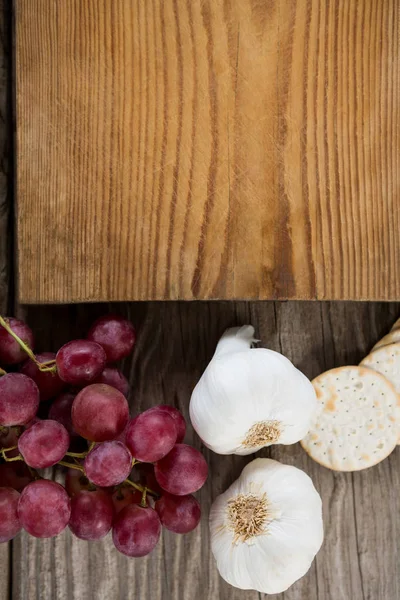 Knoflook, druiven, cracker koekje en snijplank — Stockfoto