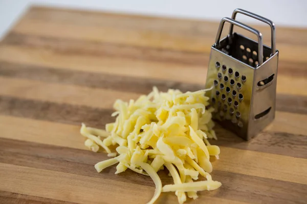 Grated cheese and grater on wooden board — Stock Photo, Image