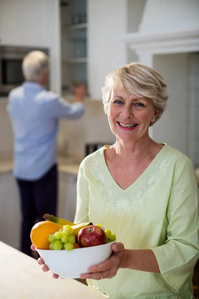 Happy senior woman holding a bowl of fruits — Stock Photo, Image