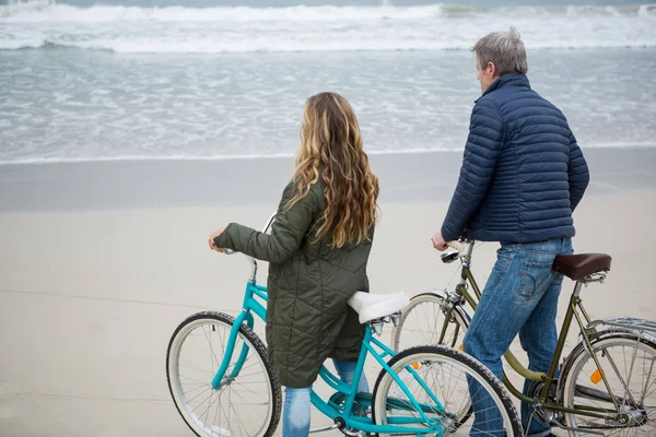 Pareja de pie con bicicleta en la playa — Foto de Stock