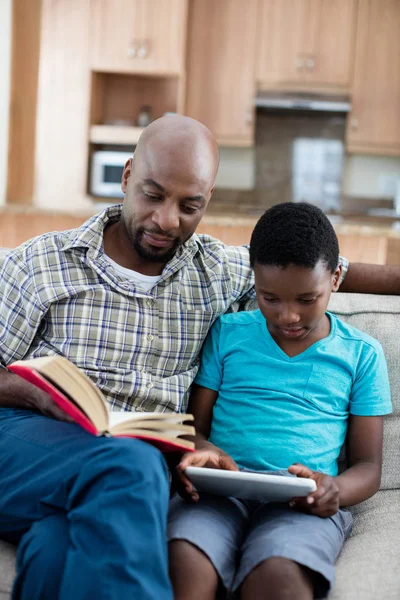 Vater liest Buch, während Sohn Tablet nutzt — Stockfoto