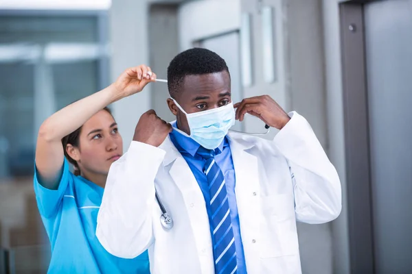 Enfermera ayudando al médico a ponerse una máscara quirúrgica — Foto de Stock