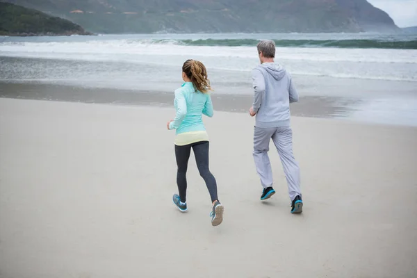 Bakifrån av par jogging på stranden — Stockfoto