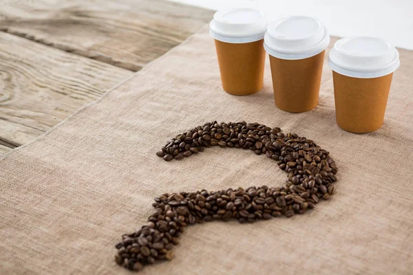 Koffiebonen gerangschikt in kwestie mark vorm met wegwerp koffie kopjes — Stockfoto