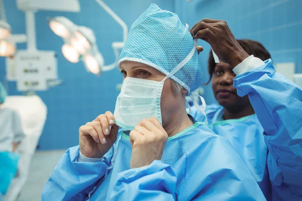 Chirurg hilft ihrem Kollegen beim Tragen einer Chirurgenmaske — Stockfoto