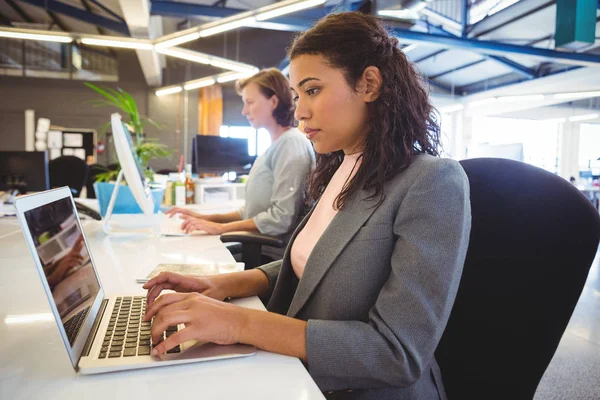 Mujer sentada en el escritorio y trabajando en el portátil — Foto de Stock