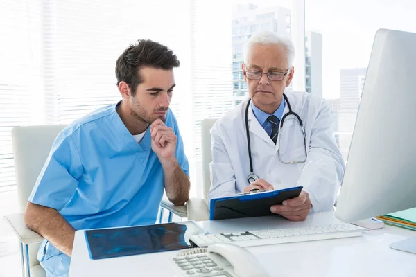 Surgeon and doctor discussing over clipboard — Stock Photo, Image