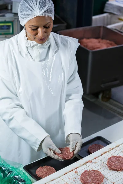 Female butcher arranging hamburger patty — Stock Photo, Image