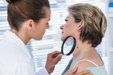 Dermatologist examining mole with magnifying glass clipart