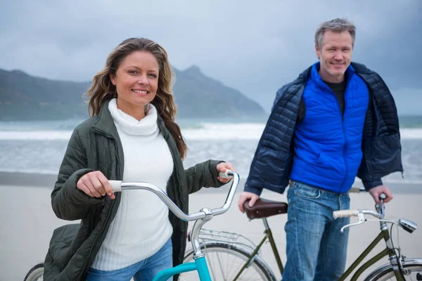 Coppia in piedi con bicicletta sulla spiaggia — Foto Stock