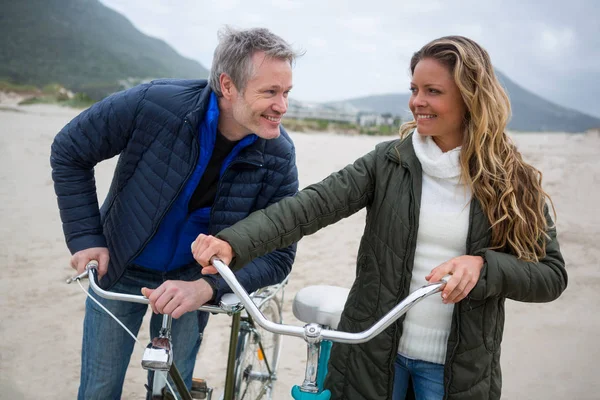 Pareja de pie con bicicleta en la playa — Foto de Stock