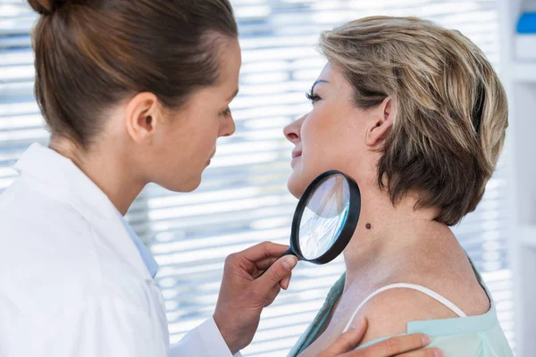 Dermatologist examining mole with magnifying glass — Stock Photo, Image