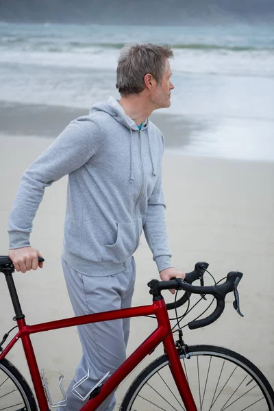 Вдумчивый человек, стоящий с велосипедом на пляже — стоковое фото