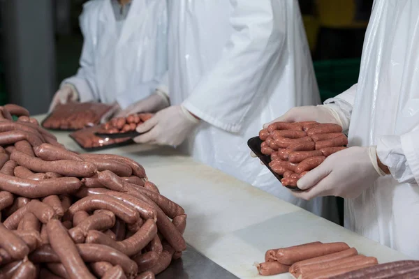 Açougueiros embalando salsichas cruas — Fotografia de Stock