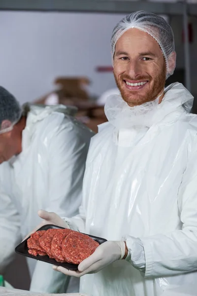 Butcher drží syrové maso placičky uspořádány v zásobníku — Stock fotografie