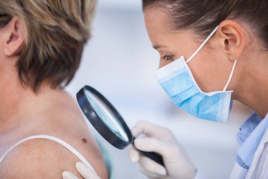 Dermatologist examining mole of female patient  clipart
