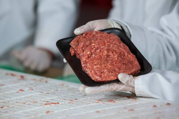 Butcher drží syrové maso placičky uspořádány v zásobníku — Stock fotografie
