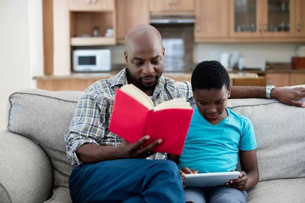Ο πατέρας ανάγνωση βιβλίων ενώ γιος χρησιμοποιώντας tablet — Φωτογραφία Αρχείου