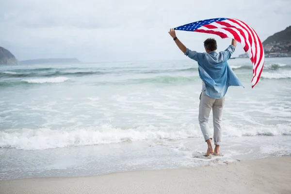 Man håller amerikanska flaggan på stranden — Stockfoto