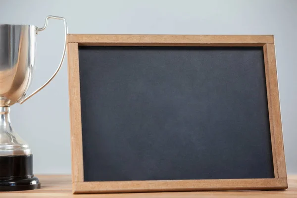 Trophy and chalkboard on wooden table — Stock Photo, Image