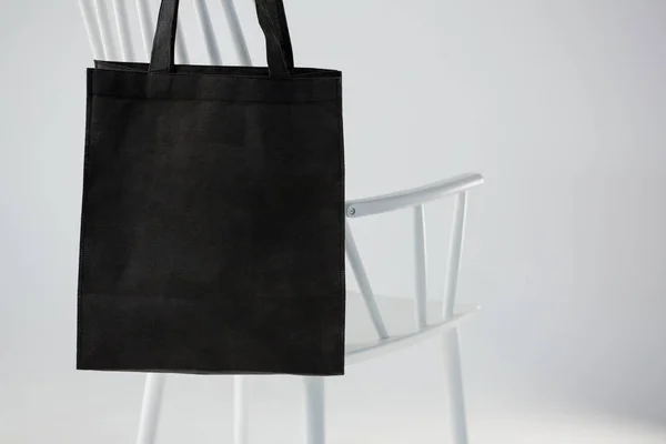 Beyaz bir sandalyeye asılı siyah çanta — Stok fotoğraf