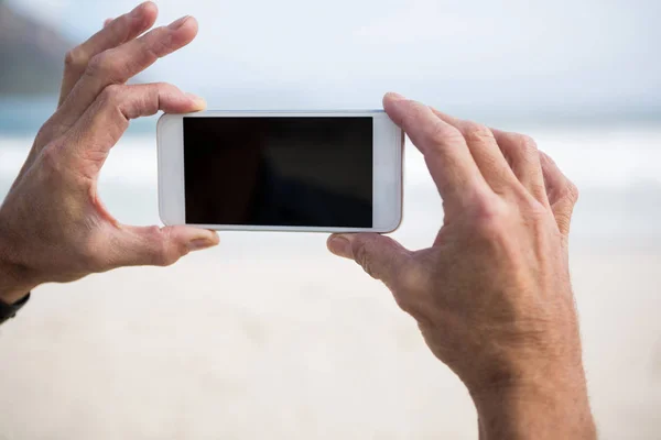 Mans hand vyfotit na telefonu na pláži — Stock fotografie