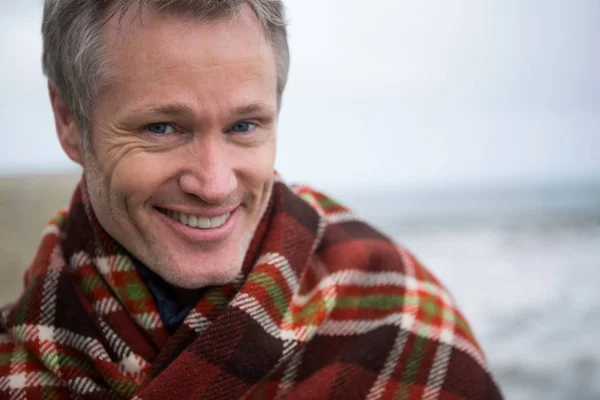 Glimlachende man verpakt in sjaal op het strand — Stockfoto