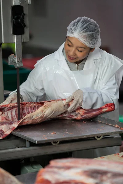 Carniceiro fêmea cortando carne crua — Fotografia de Stock