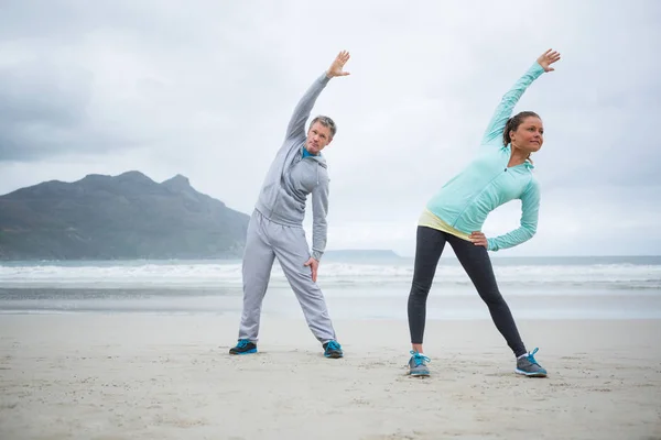 Couple effectuant des exercices d'étirement sur la plage — Photo