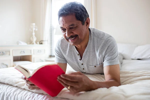 Homme âgé souriant lisant un roman — Photo