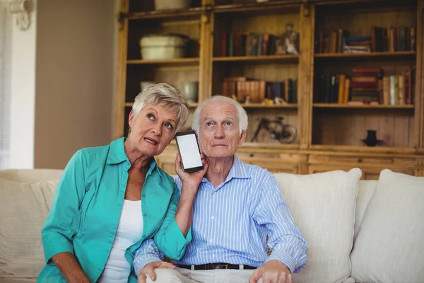 Äldre par med telefon i vardagsrum — Stockfoto