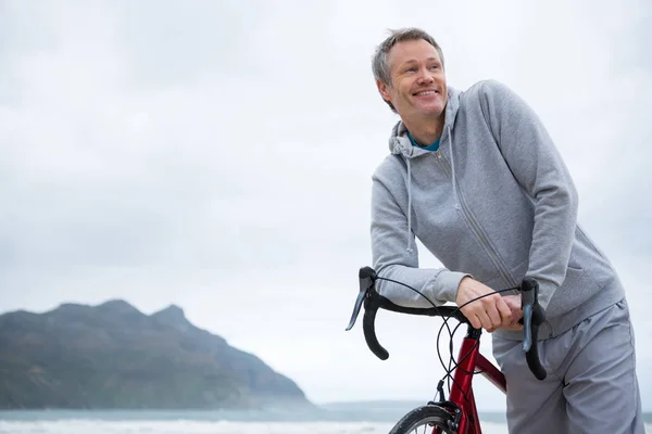 Felice uomo appoggiato sulla bicicletta in spiaggia — Foto Stock