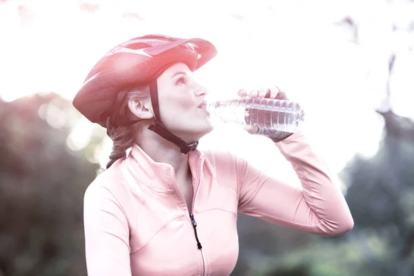 Female cyclist drinking water in forest — Stock Photo, Image