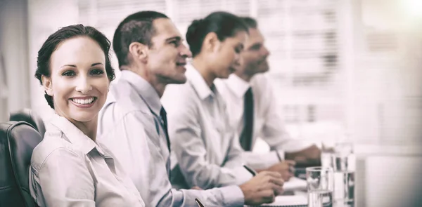 Businesswoman smiling at camera while her colleagues listening to presentation — Stock Photo, Image