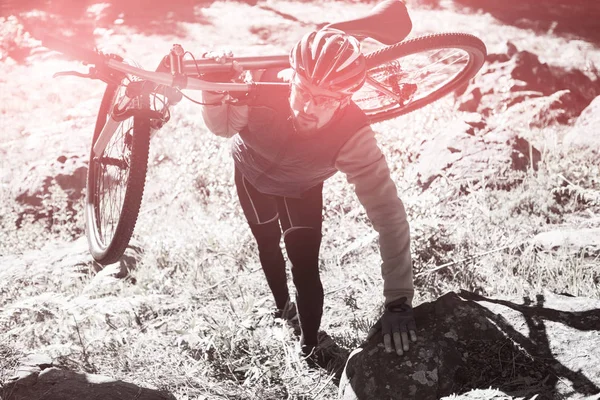 Motociclista de montanha masculino carregando bicicleta na floresta — Fotografia de Stock