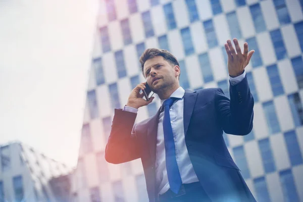 Vista de ángulo bajo del hombre de negocios haciendo gestos mientras habla por teléfono móvil — Foto de Stock
