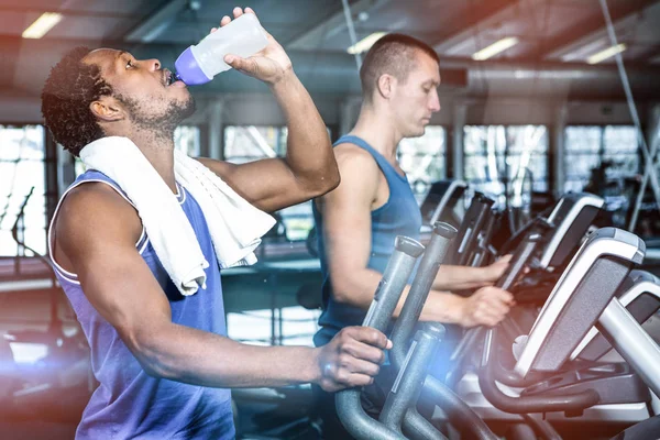 Uomo acqua potabile durante l'utilizzo di macchina ellittica — Foto Stock