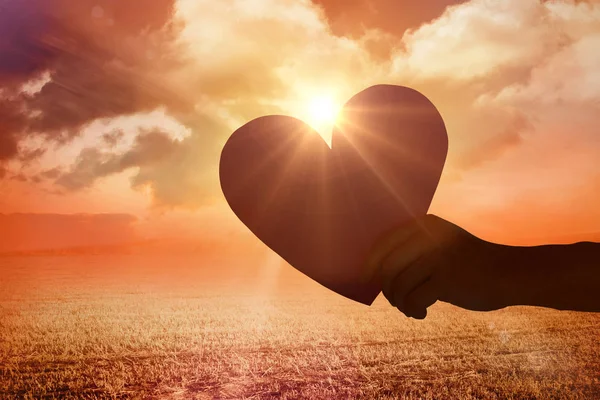 Hand holding heart against sunrise — Stock Photo, Image