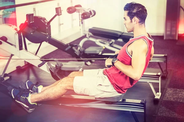 Hombre musculoso en la máquina de remo en el gimnasio