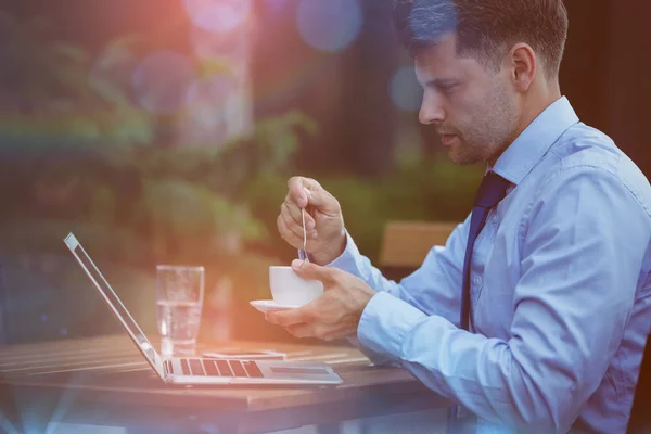 Handsome businessman holding tea while using laptop — Stock Photo, Image